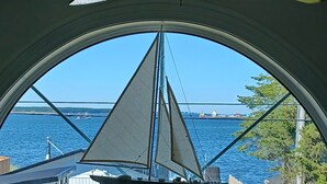 En modellsegelbåt står inne i ett rum med ett stort, välvt fönster som vetter mot en vattenyta.