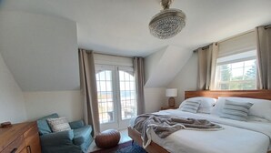 Ett sovrum med en stor säng, en byrå i trä, en blå soffa och en mönstrad matta.