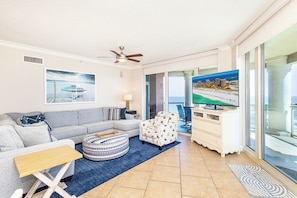 Ein Wohnzimmer mit Sofa, Hocker, Fernseher und Meerblick durch große Fenster.