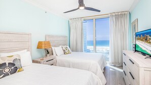 A hotel room with two beds, a ceiling fan, a TV, and a view of the ocean.