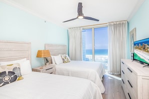 Ein Hotelzimmer mit zwei Betten, einem Deckenventilator, einem Fernseher und Blick auf das Meer.
