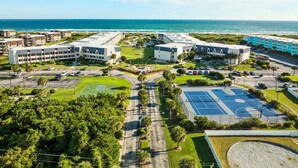 Un complexe hôtelier situé sur la côte, composé de plusieurs bâtiments, de zones de stationnement et d’un terrain de sport.