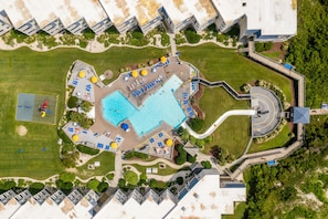 An aerial view of a resort with a central swimming pool, multiple lounge areas, and a playground.
