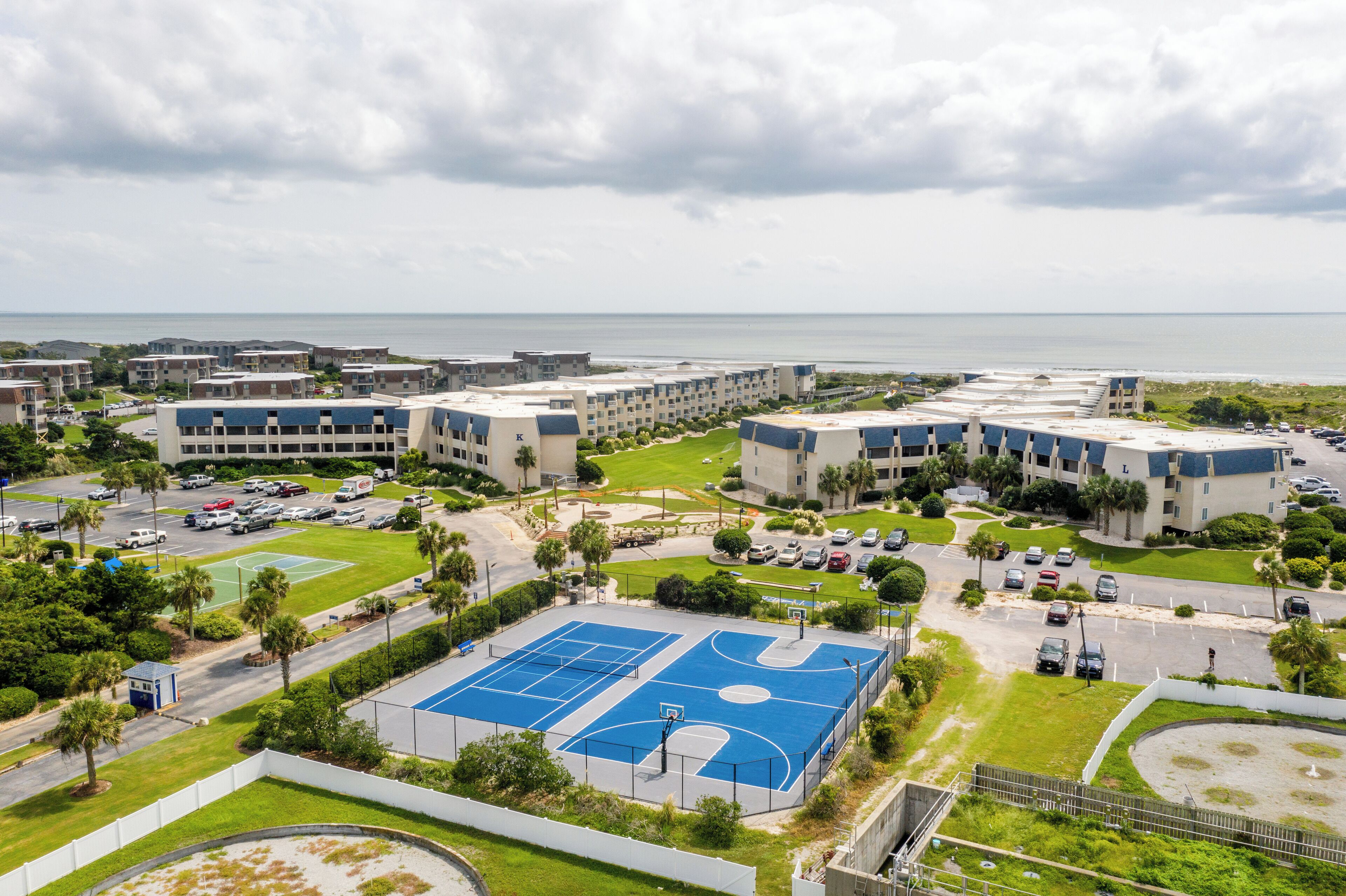 A residential area with multiple apartment buildings, a basketball court, and a view of the ocean.