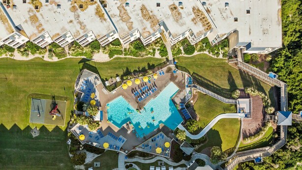 Vue aérienne d’un complexe hôtelier doté d’une piscine centrale, de nombreuses chambres et d’un espace paysager agrémenté de sentiers et de verdure.