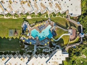 An aerial view of a resort with a central swimming pool, multiple guest rooms, and a landscaped area with pathways and greenery.