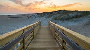 Une promenade en bois menant à une plage, avec un coucher de soleil en arrière-plan.