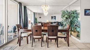 Een eetgedeelte met een grote tafel, zes stoelen, een kroonluchter en een grote potplant.