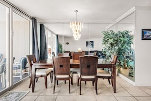 Un comedor con una mesa grande y seis sillas, una araña y una planta en maceta.