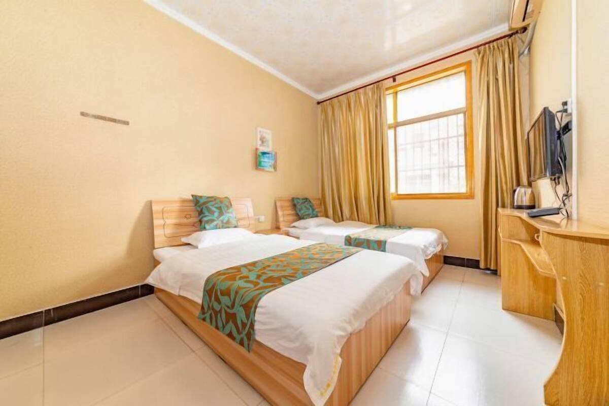 Een hotelkamer met twee bedden, een houten bureau, een raam met gordijnen en een kleine tv aan de muur.