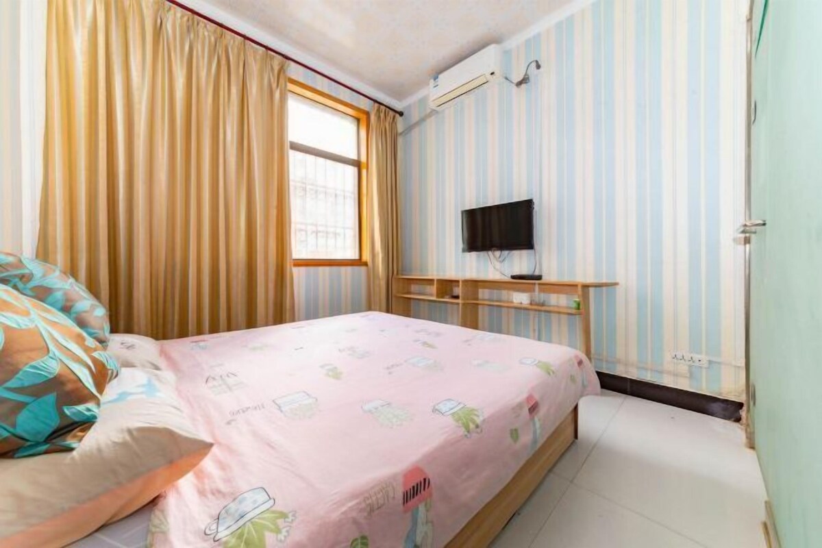 A bedroom with a bed, a television on a shelf, and a window with curtains.