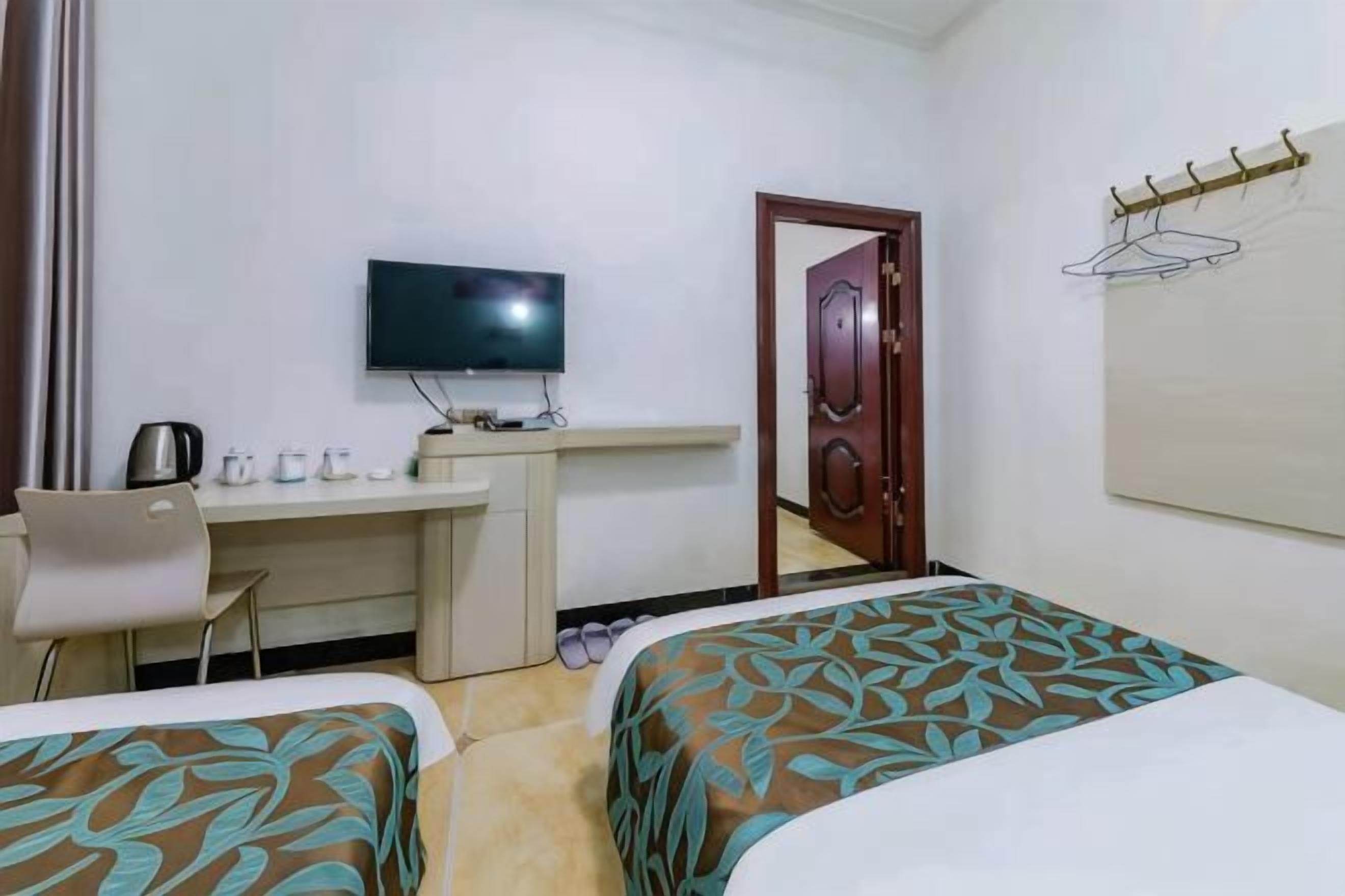 A hotel room with two beds, a desk with a television, and a door.