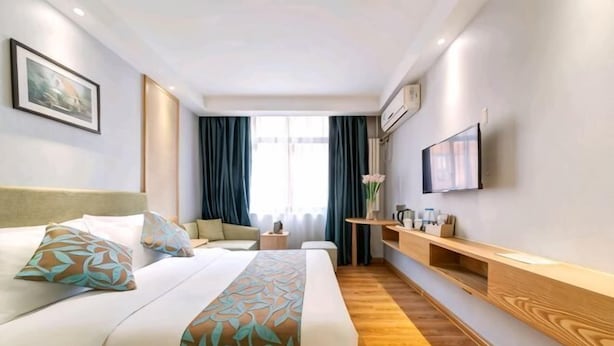 Una habitación de hotel con cama, televisión, escritorio y ventana con cortinas.