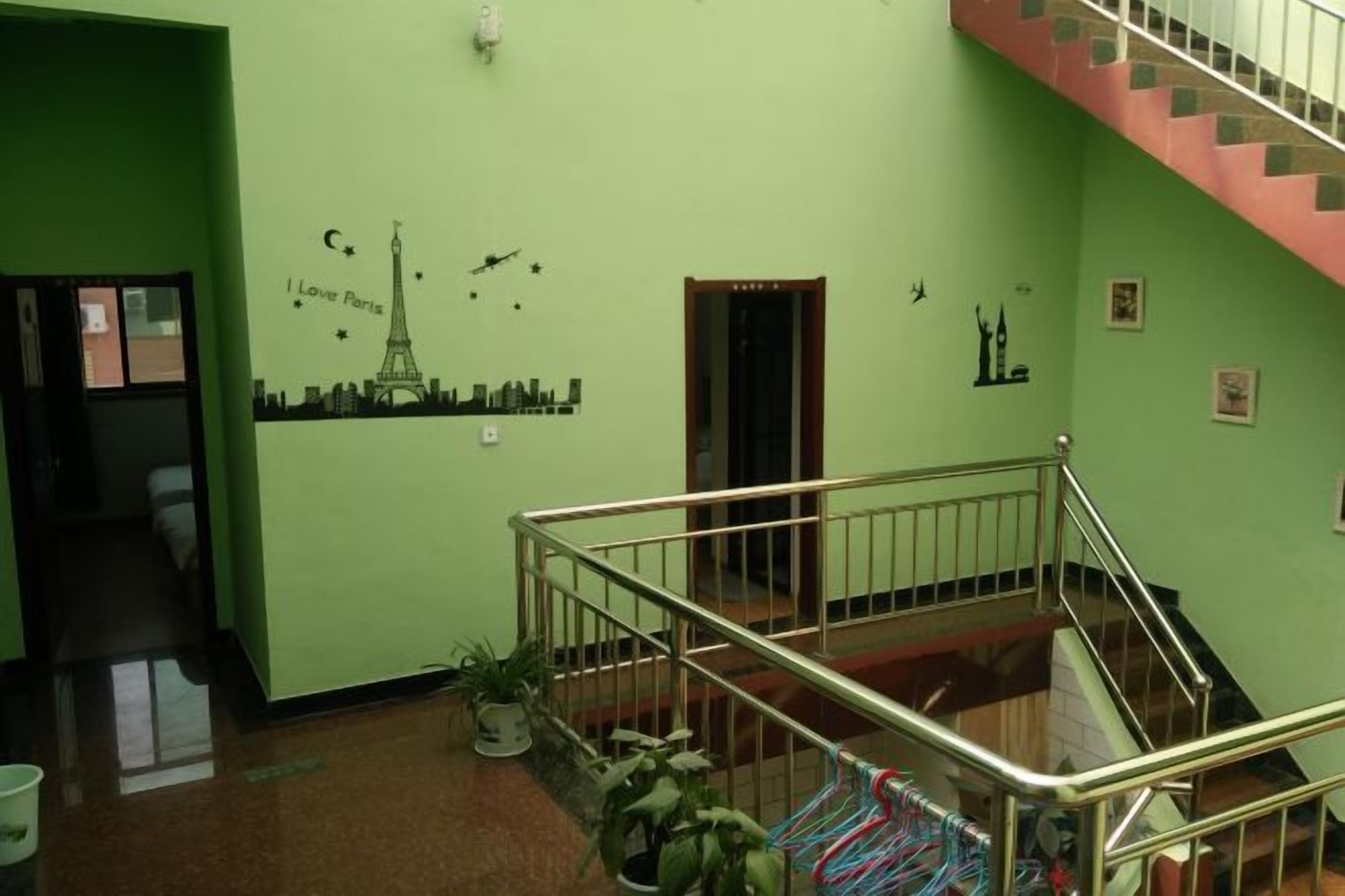 Un intérieur aux murs verts, avec un escalier, une porte et un mur décoré d’autocollants représentant un paysage urbain.