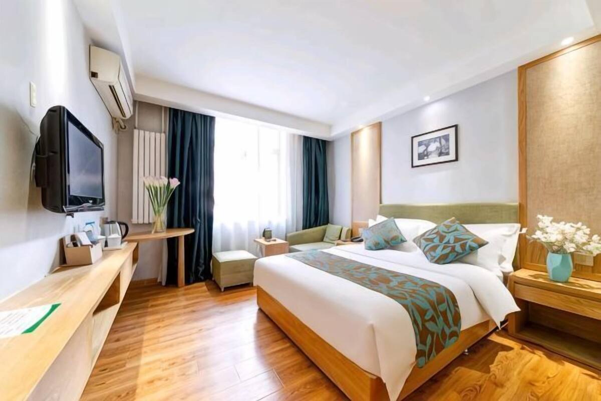 Hotelkamer met een bed, een bureau, een televisie, een raam met gordijnen en een schilderij aan de muur.