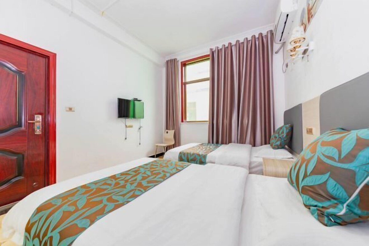 A hotel room with two beds, a TV, a window with curtains, and a red door.
