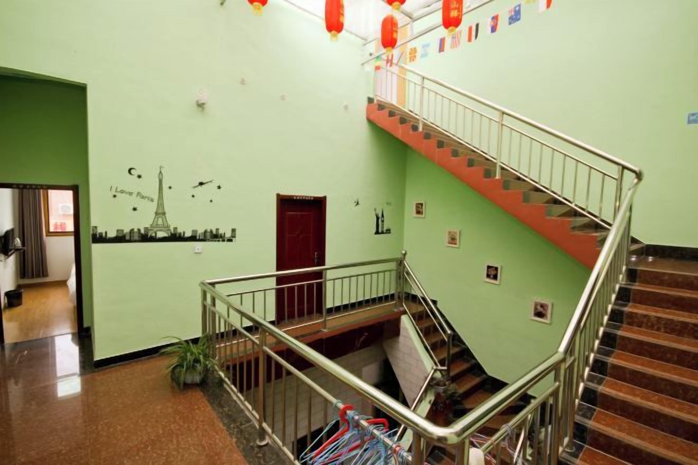 A hotel lobby with a staircase, a red door, and a green wall with Eiffel Tower and other cityscape decorations.