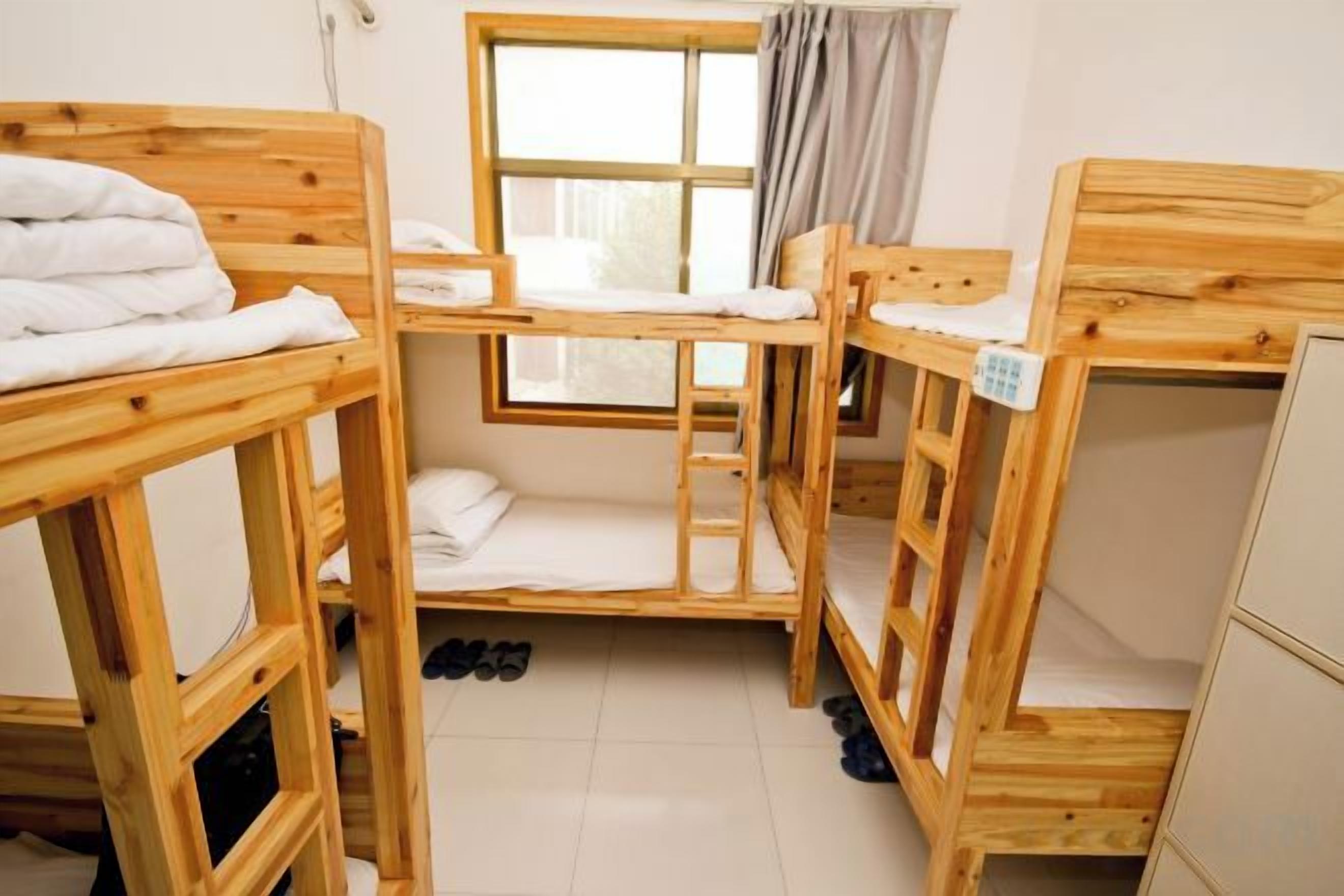 Une chambre avec des lits superposés, une fenêtre avec des rideaux et un petit placard.