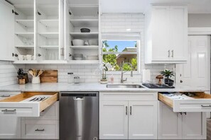 Een moderne keuken met witte kastjes, een RVS vaatwasser en een raam met uitzicht op groen.