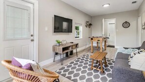 Un salon avec un canapé, une table basse, un téléviseur fixé au mur et un jeu de fléchettes.