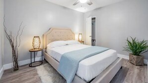 Une chambre à coucher avec un lit, des lampes de chevet, un ventilateur de plafond, une plante et une porte.