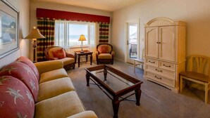 A living room with a sofa, armchairs, a coffee table, a lamp, a cabinet, and a view of the ocean. - Sandcastle Court #220 -Kitchen (Nassau County)
