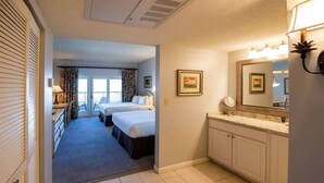 A hotel room with two beds, a bathroom with a large mirror and vanity, and a hallway leading to another room. - Sandcastle Court #220 -Kitchen (Nassau County)