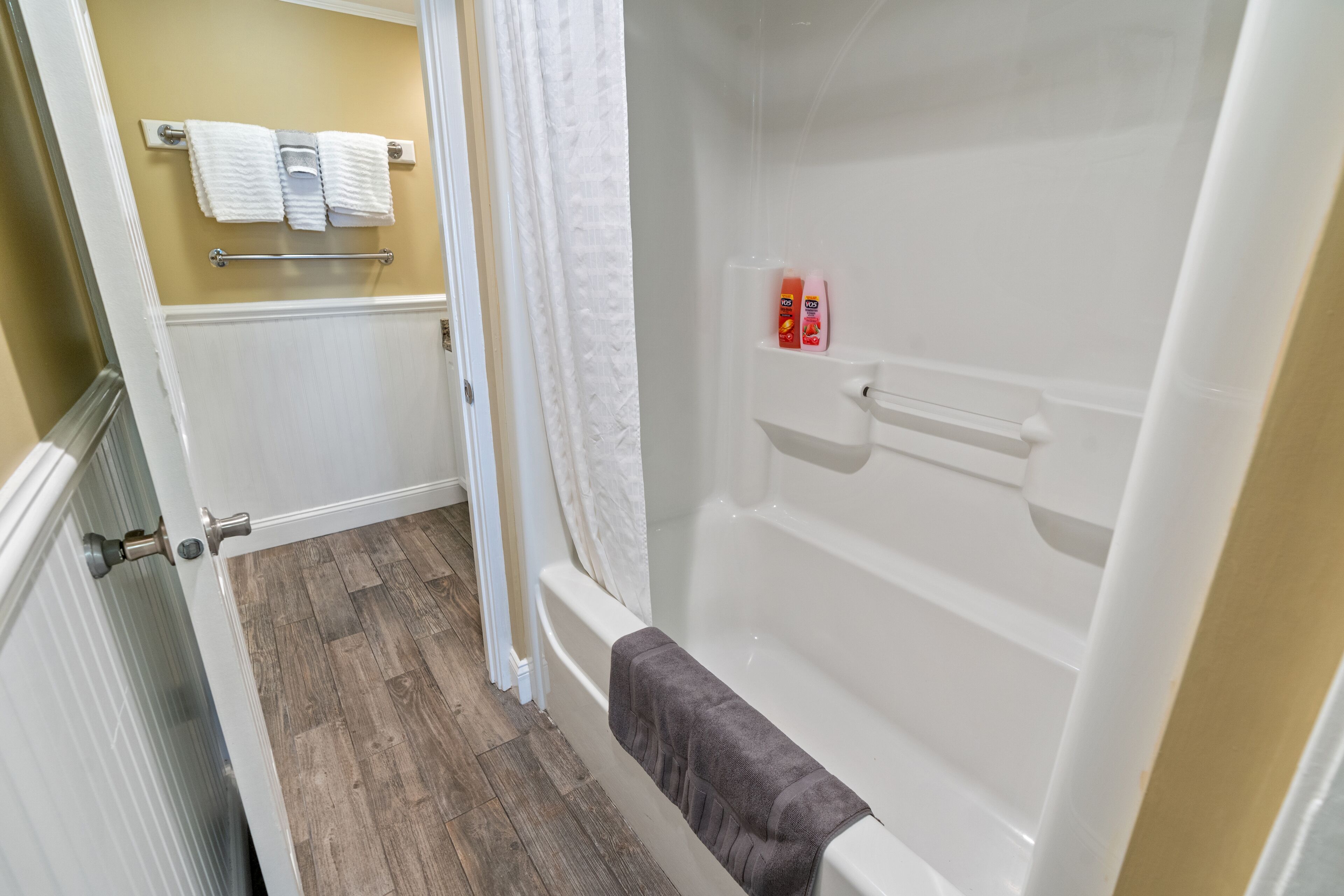 A bathroom with a bathtub, a towel rack with two towels, and a shower curtain.