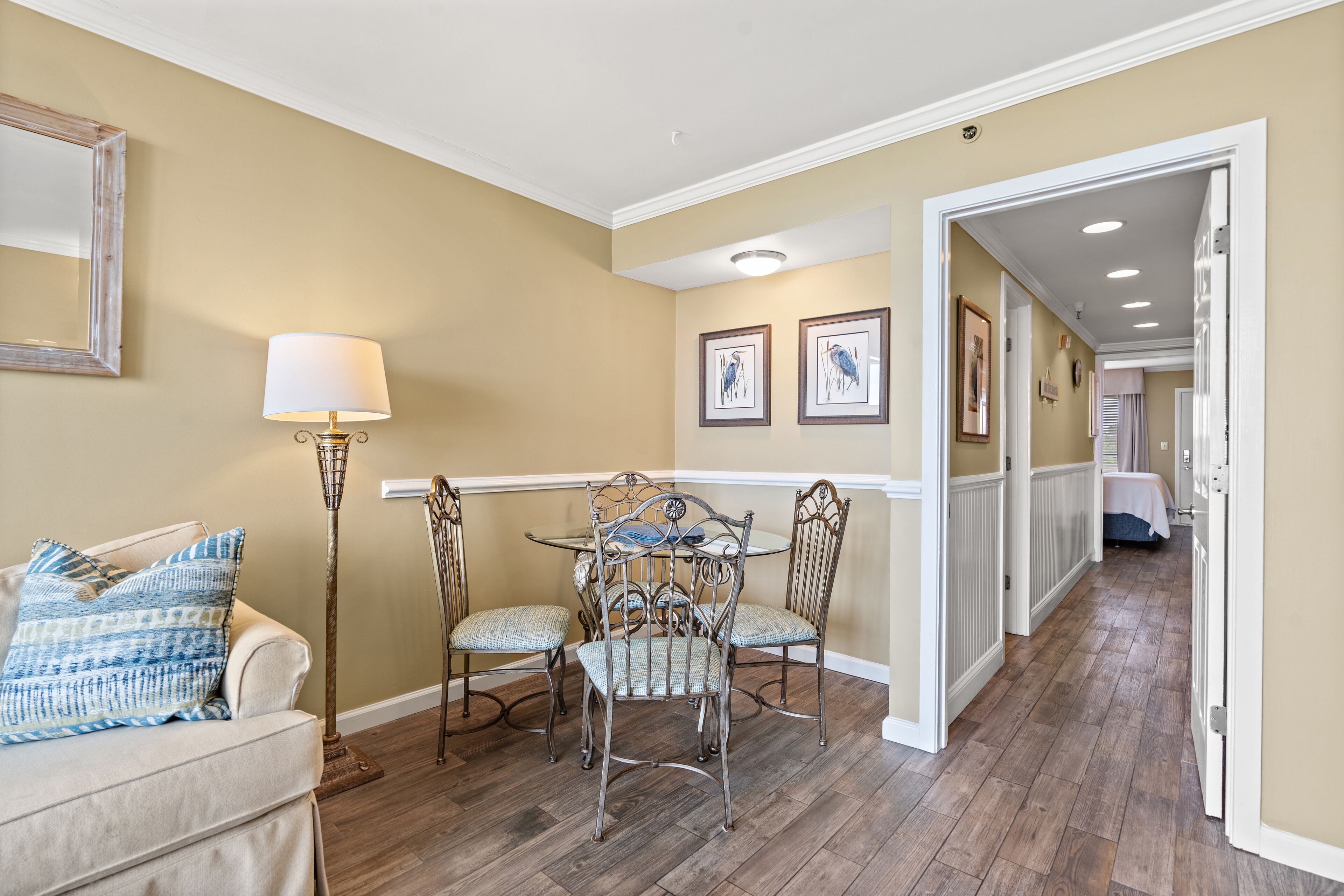 A dining area with a table and chairs, a lamp, and framed pictures on the wall.