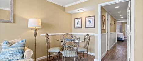 A dining area with a table and chairs, a lamp, and framed pictures on the wall.