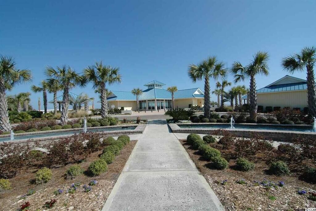 A hotel entrance with a central pathway flanked by palm trees and a water feature.