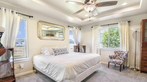 Une chambre avec un grand lit, un ventilateur de plafond, un miroir et une vue sur l’extérieur.