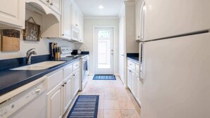 A narrow kitchen with white cabinets, a black countertop, and a door at the end. - Fairway Oaks 3209 (Fernandina Beach)