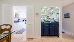 A modern kitchen with white and dark blue cabinets, a glass display case, and a dining area with a glass table and wooden chairs. - Fairway Oaks 3209 (Fernandina Beach)