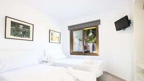 A hotel room with two beds, a TV mounted on the wall, and a window with a view of the outside. - GOLETA - Just 40 mts from the beach! (Port de Pollença)