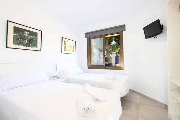 A hotel room with two beds, a TV mounted on the wall, and a window with a view of the outside. - GOLETA - Just 40 mts from the beach! (Port de Pollença)