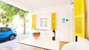 A room with a table, chairs, a bowl of fruit, a bottle of wine, and a window with yellow shutters. - GOLETA - Just 40 mts from the beach! (Port de Pollença)