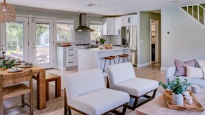 A modern kitchen with white cabinets, a central island, and bar stools. There is a dining area with a wooden table and chairs, and a living area with a sofa and a coffee table. - Re-modernized home with heated saltwater pool, home office, gym, electric... (Southampton)