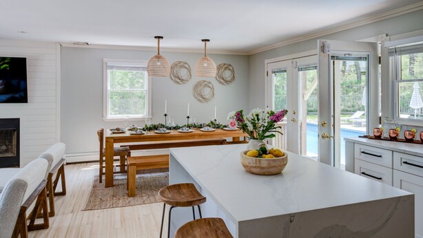 A modern kitchen with a large island, wooden dining table, pendant lights, and a view of the outdoors. - Re-modernized home with heated saltwater pool, home office, gym, electric... (Southampton)