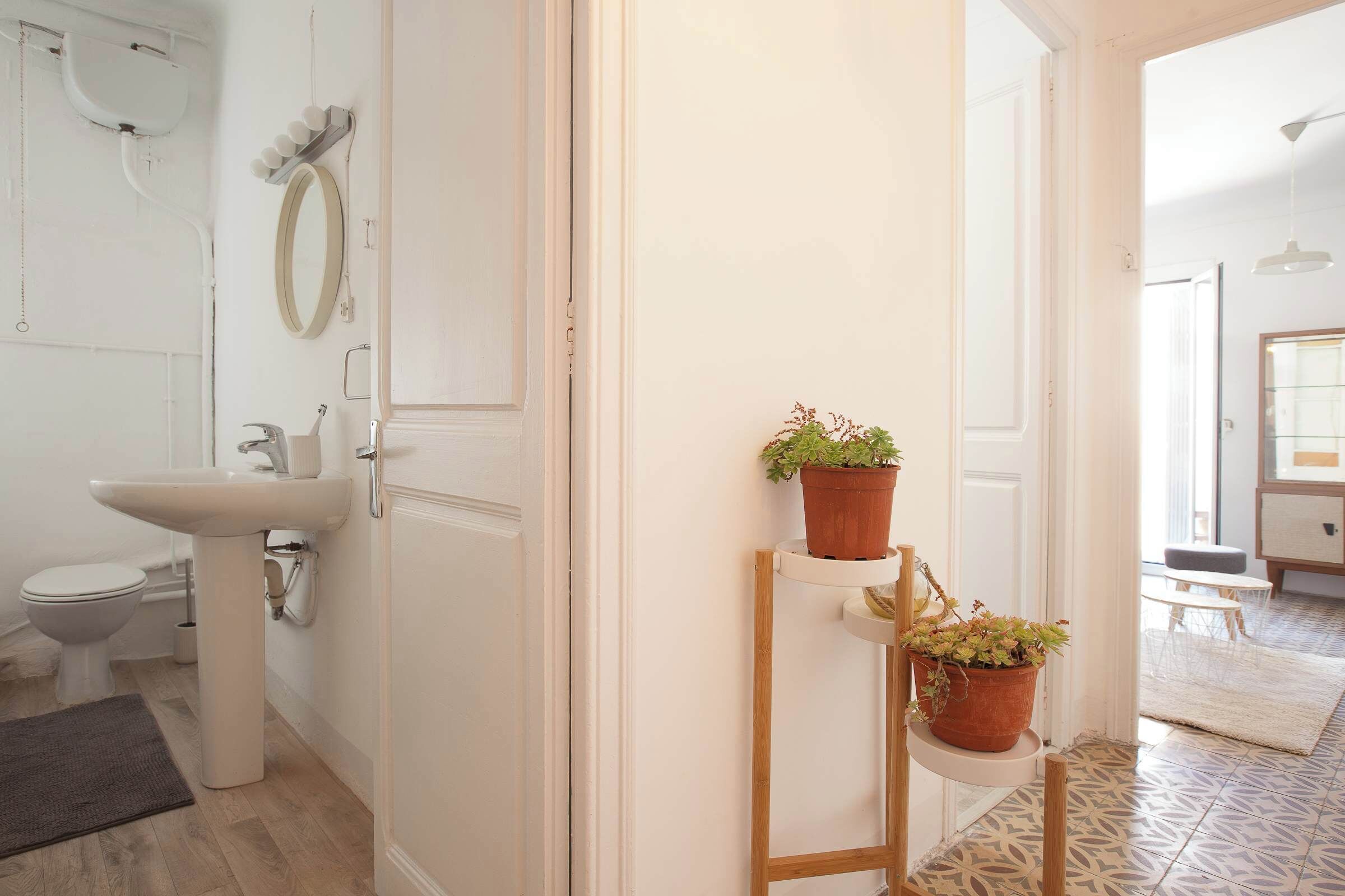 Ein Badezimmer mit Toilette, Waschbecken und Spiegel. Auf einem Regal stehen zwei Blumentöpfe.