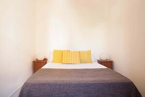 A neatly made bed with a grey blanket and three yellow pillows. There are two bedside tables with white lamps. - Monumental Apartment located in L’Eixample (Barcelona)