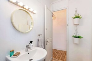 A bathroom with a round mirror, a sink, and two hanging plants. - Monumental Apartment located in L’Eixample (Barcelona)