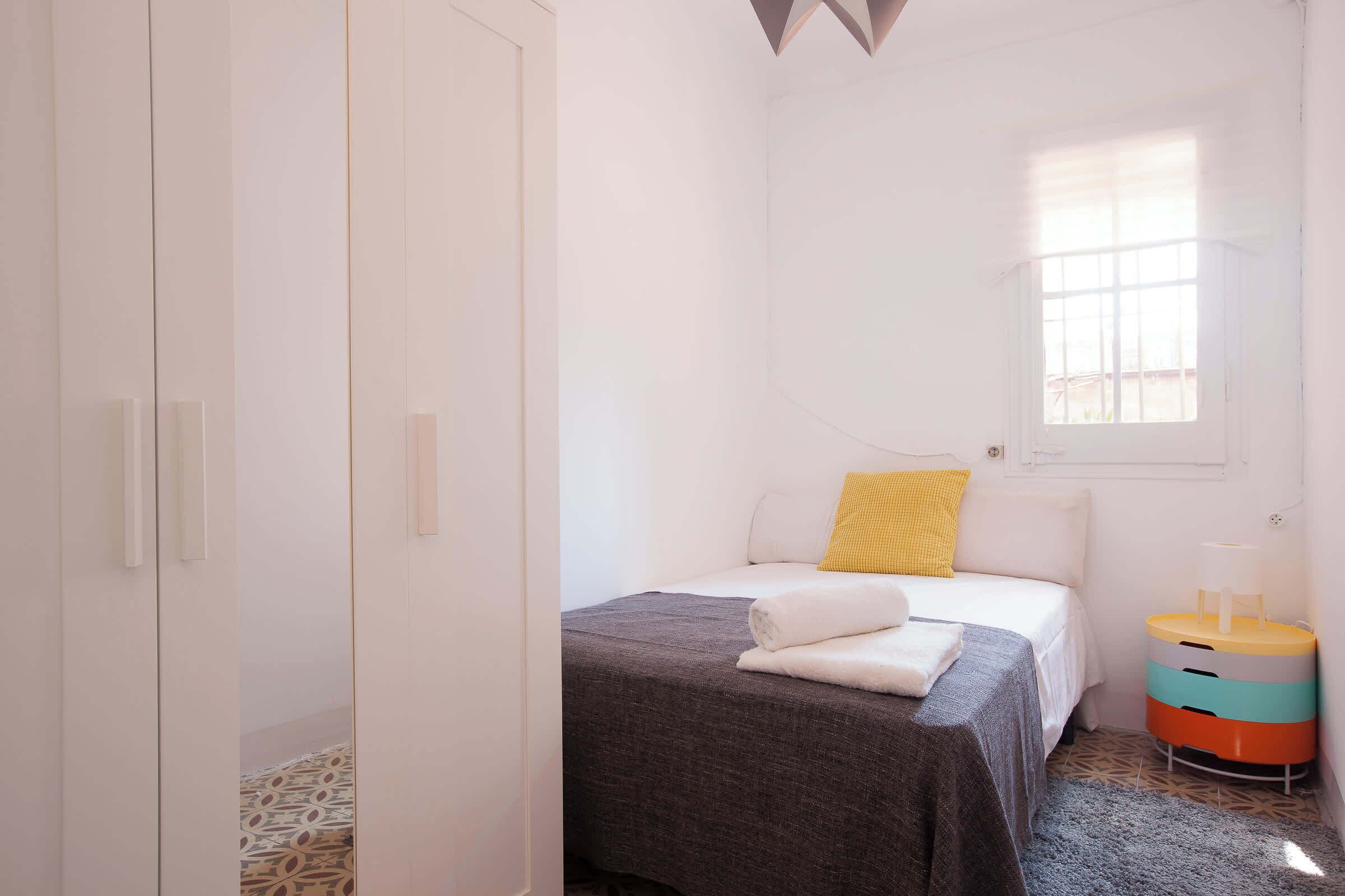 A bedroom with a bed, a bedside table, a window, and a wardrobe.