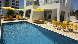 A modern pool area with a clear blue pool, yellow lounge chairs, and umbrellas.