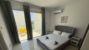 A modern bedroom with a large bed, a nightstand, an air conditioning unit, and a view of the outside balcony.