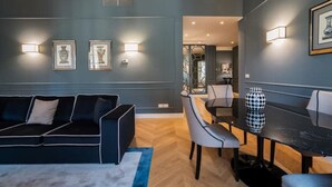Un salon moderne avec un canapé bleu foncé, une table à manger avec des chaises et des luminaires fixés au mur.