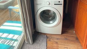 A compact laundry room with two stacked washing machines, a wooden floor, and a view of the outdoors through a window.