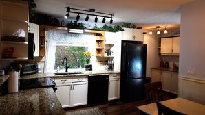 A kitchen with white cabinets, a black refrigerator, a coffee maker, and a window with a view of trees.