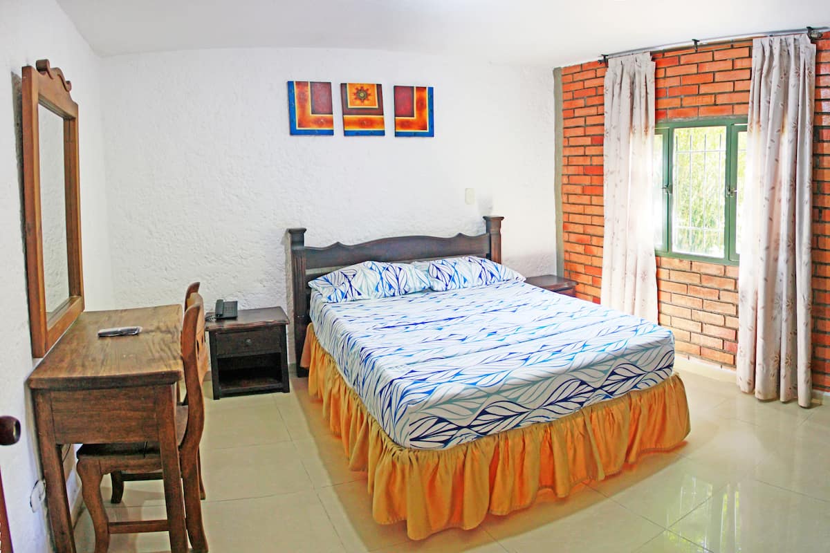 A bedroom with a bed, a desk, a chair, a wardrobe, and a window with curtains.