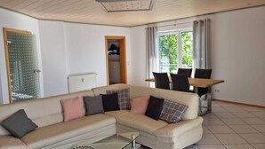 A modern living room with a beige sectional sofa, a glass coffee table, and a dining area with a wooden table and chairs. - Ferienwohnung "schöne Aussicht" in der Rhön (Kalbach)